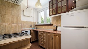 A kitchen with a gas stove, a built-in oven, a white refrigerator, wooden cabinets, and a window with a view of greenery outside. - Złota Heart of Warsaw Apartment (Warszawa)