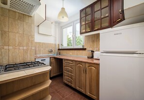 A kitchen with a gas stove, a built-in oven, a white refrigerator, wooden cabinets, and a window with a view of greenery outside. - Złota Heart of Warsaw Apartment (Warszawa)
