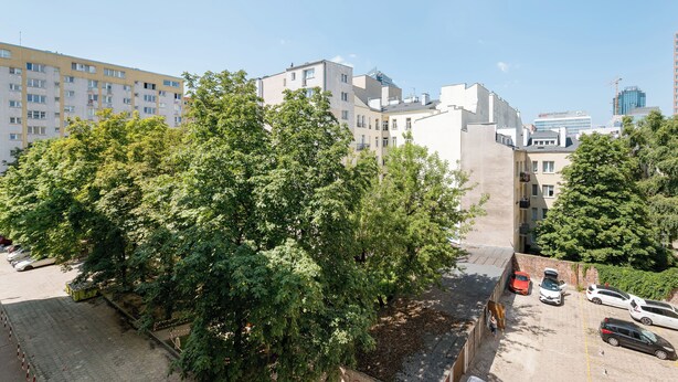 A multi-story residential building with a parking area and trees in the foreground. - Złota Heart of Warsaw Apartment (Warszawa)