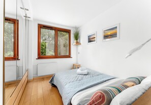 A bedroom with a bed, a window, a plant, and a picture on the wall. - Dembowskiego Cosy Nest Apartment (Kraków)