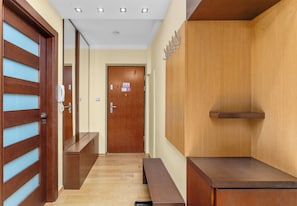 A hallway with wooden doors, a bench, a reception desk, and a wall-mounted shelf. - Dembowskiego Cosy Nest Apartment (Kraków)