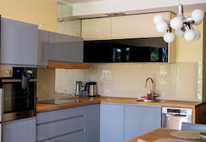A modern kitchen with built-in appliances, a wooden countertop, and a stainless steel dishwasher. - Dembowskiego Cosy Nest Apartment (Kraków)