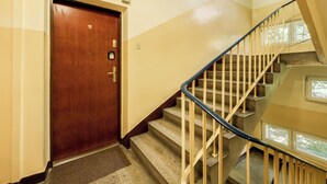 Una puerta de madera con una placa de número, una escalera con barandilla de metal y un rellano alfombrado.