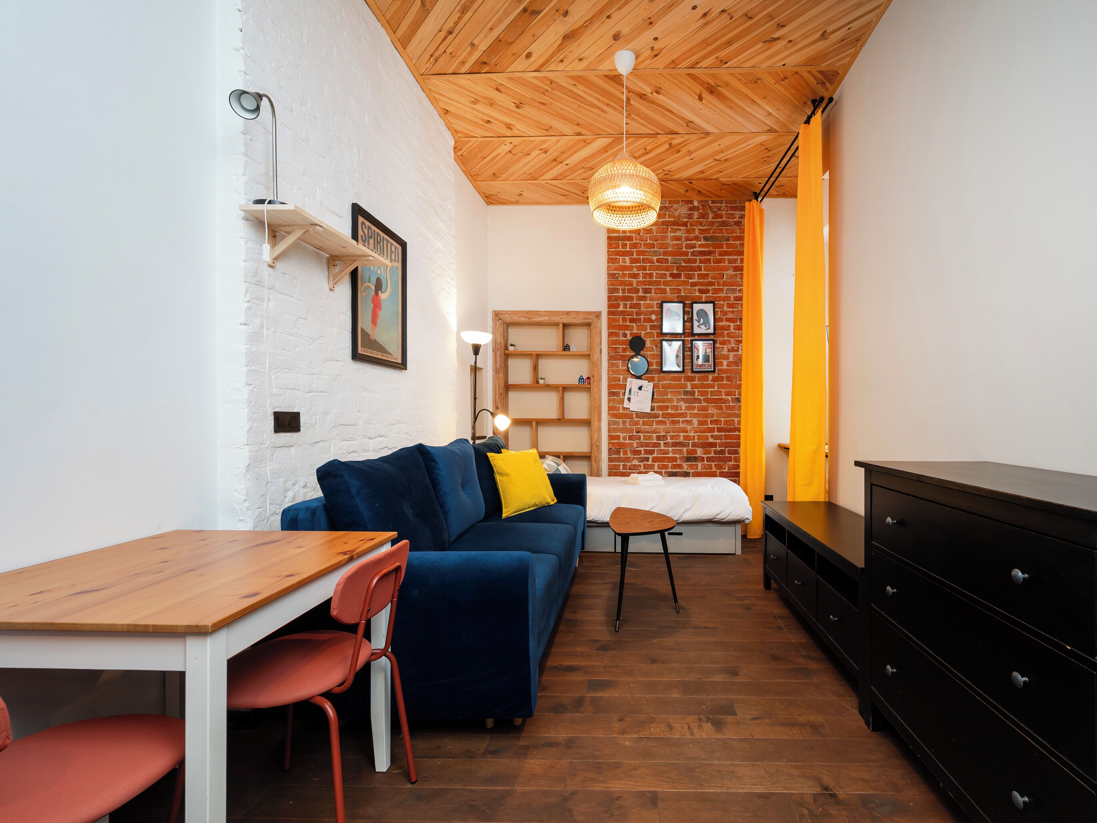 A compact living space with a wooden ceiling, a blue sofa, a wooden table, and a black dresser.