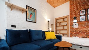A room with a blue sofa, a small wooden table, a white bed, a brick wall, and a framed poster on the wall. - Kościuszki Prime Studio (Łódź)