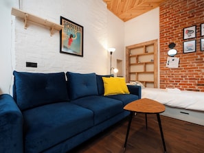 Ein Zimmer mit einem blauen Sofa, einem kleinen Holztisch, einem weißen Bett, einer Ziegelwand und einem gerahmten Poster an der Wand.