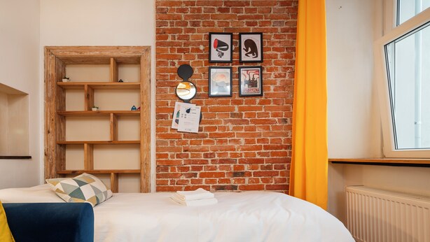 A room with a brick wall, a bed with white bedding, a blue sofa, and a window with a view. - Kościuszki Prime Studio (Łódź)