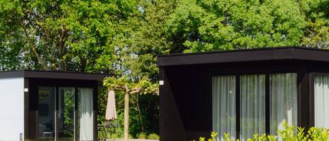 Two modern cabins with large windows, surrounded by lush greenery and trees.
