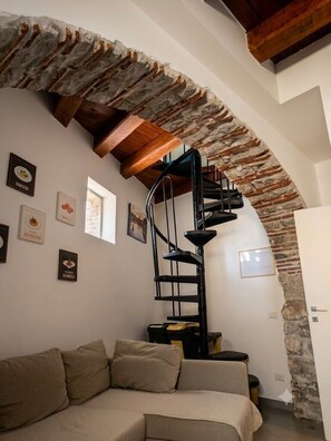 Eine Wendeltreppe mit einem steinernen Bogen, ein beiges Sofa und gerahmte Bilder an der Wand.