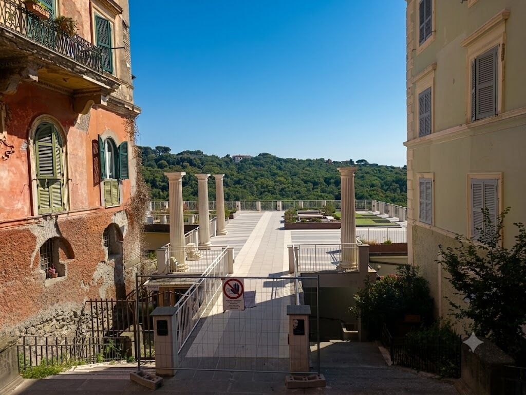 A street view with a gate, buildings, and a hill in the background.