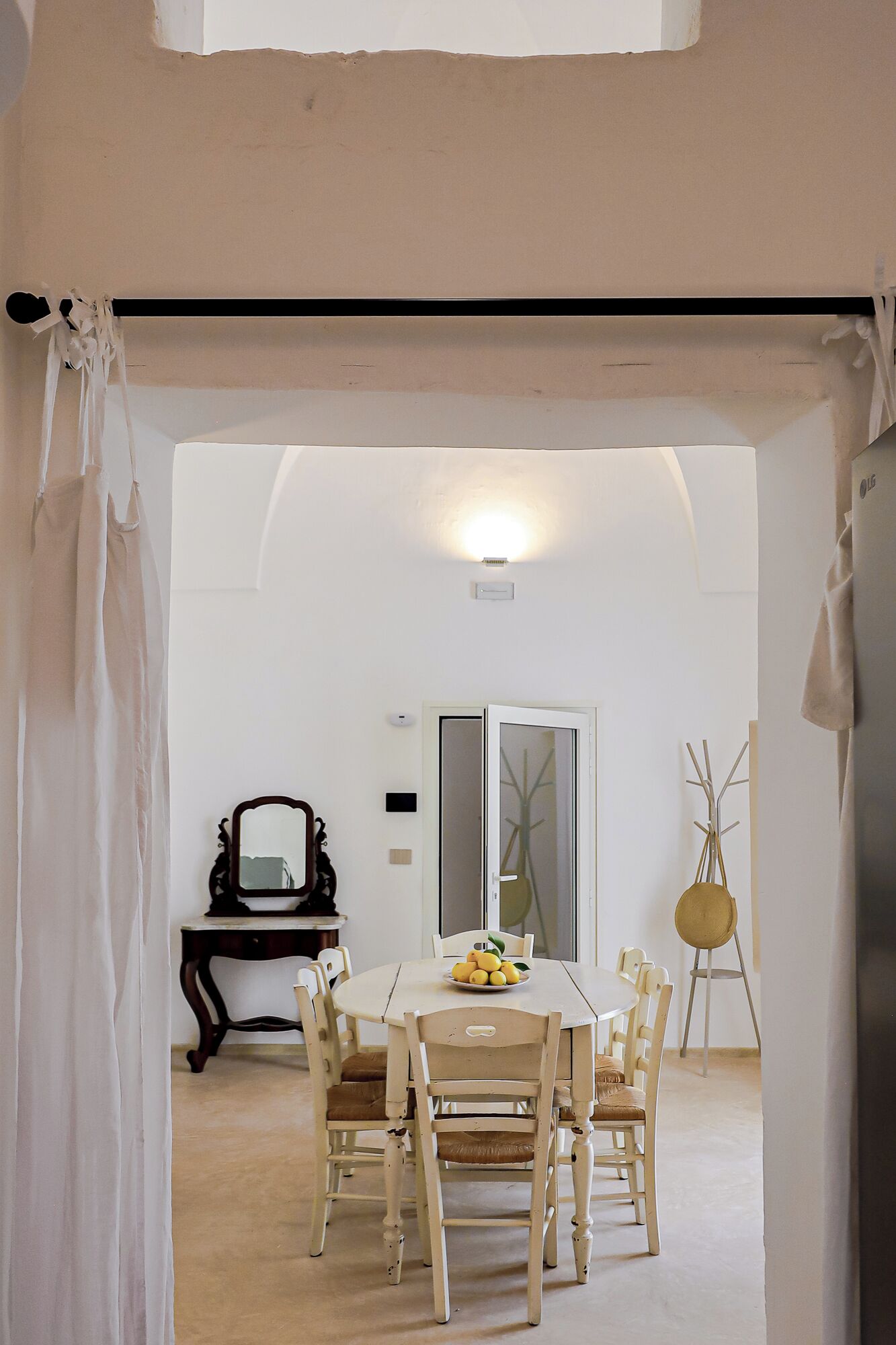 A dining area with a table, chairs, a mirror, and a vase with branches.