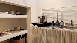 Cocina con lavabo, estufa y utensilios. Hay una ventana sobre el lavabo y una repisa con recipientes.