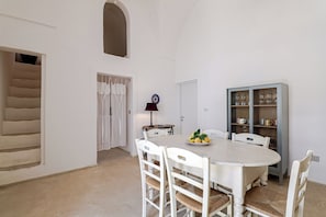 Une salle à manger avec une table ronde, des chaises blanches, un buffet contenant de la verrerie et une porte avec une fenêtre.