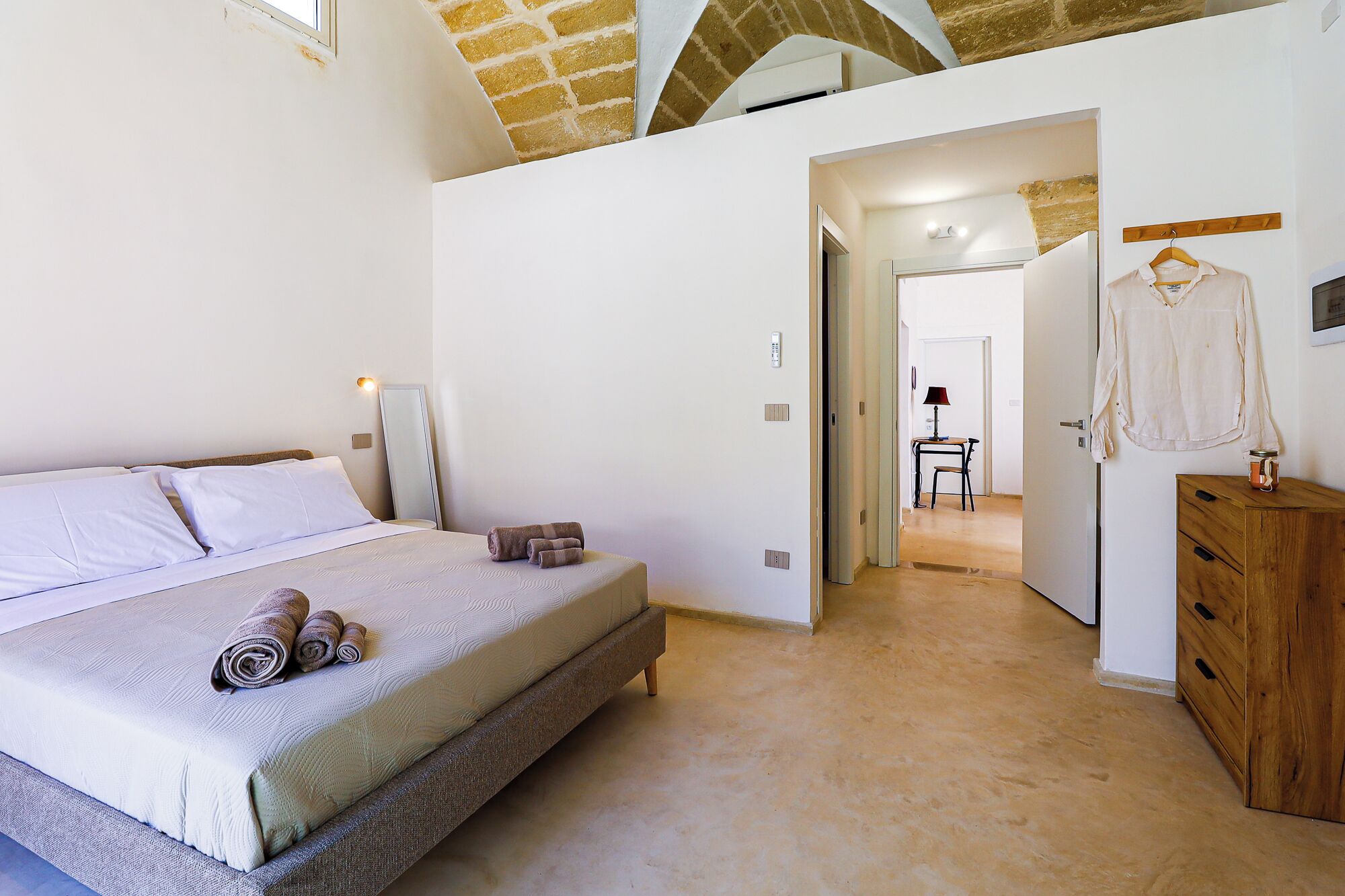 Une chambre à coucher avec un lit, une commode en bois et un couloir menant à une autre pièce.