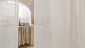 Un pasillo estrecho con una cortina blanca, un lavabo y una ventana.