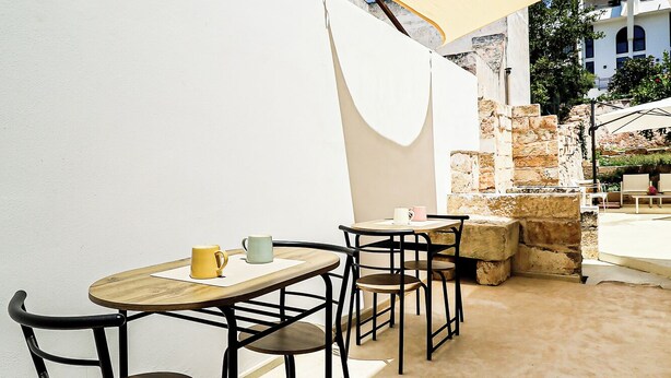 Un patio al aire libre con una mesa redonda y sillas, un paraguas amarillo y un muro de piedra.