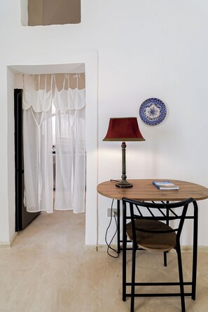 Une pièce comprenant une table ronde en bois, une seule chaise, une lampe, une assiette décorative et une porte surmontée de rideaux légers.