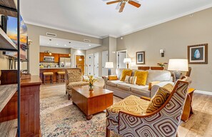 A living room with a sofa, chairs, a coffee table, and a kitchen in the background. - Maui Resort Rentals: Two Luxury Ground Floor Suites with Expansive Lawns Near Beach, Pools and BBQs! (Lahaina)