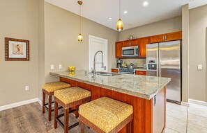 Eine Küche mit Granit-Arbeitsplatte, Edelstahlgeräten, Holzschränken und einer Bar mit Sitzgelegenheiten.