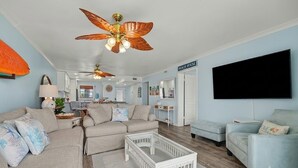 Uma sala de estar com ventilador de teto, televisão e uma placa com a inscrição 'BEACH HOUSE'.
