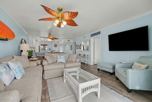 Ein Wohnzimmer mit Deckenventilator, einem Fernseher und einem Schild mit der Aufschrift 'BEACH HOUSE'.