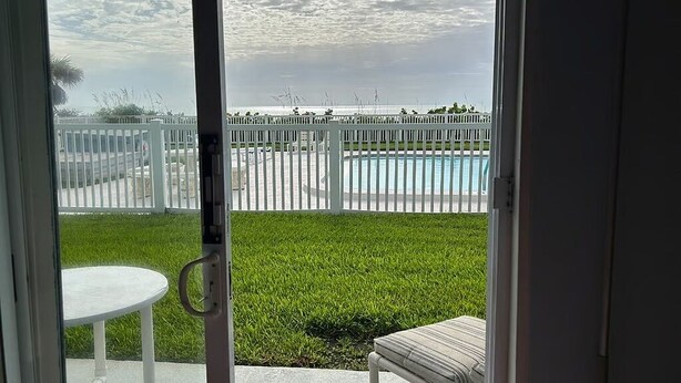 Visão através de uma porta de vidro para um quintal com piscina, cerca branca e área gramada.