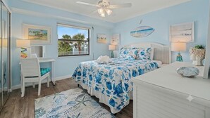 Quarto com cama, escrivaninha, cadeira, ventilador de teto e obras de arte nas paredes.
