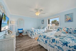Une chambre avec deux lits, un ventilateur de plafond, une grande fenêtre et une vue sur l’extérieur.