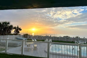 A pool area with a sunset view, white fencing, and lounge chairs. - Summer Promo Beach Deal - Oceanfront 2BR Condo, Pool, Beach Gear (Satellite Beach)