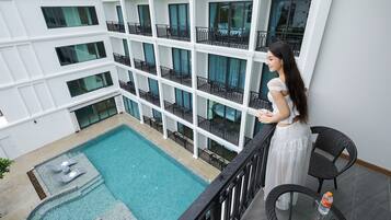 A multi-level building with a swimming pool, balconies with railings, and a person standing by a table with a chair.