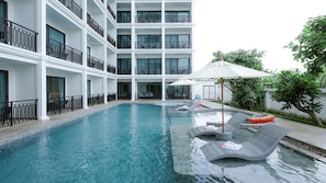 A swimming pool with lounge chairs and umbrellas, surrounded by a multi-story building with balconies. - B2 Mae Sot Premier Hotel (Mae Sot)