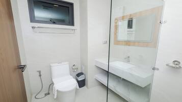 Une salle de bain moderne équipée de toilettes, d’un bidet et d’une douche séparée par une paroi en verre.
