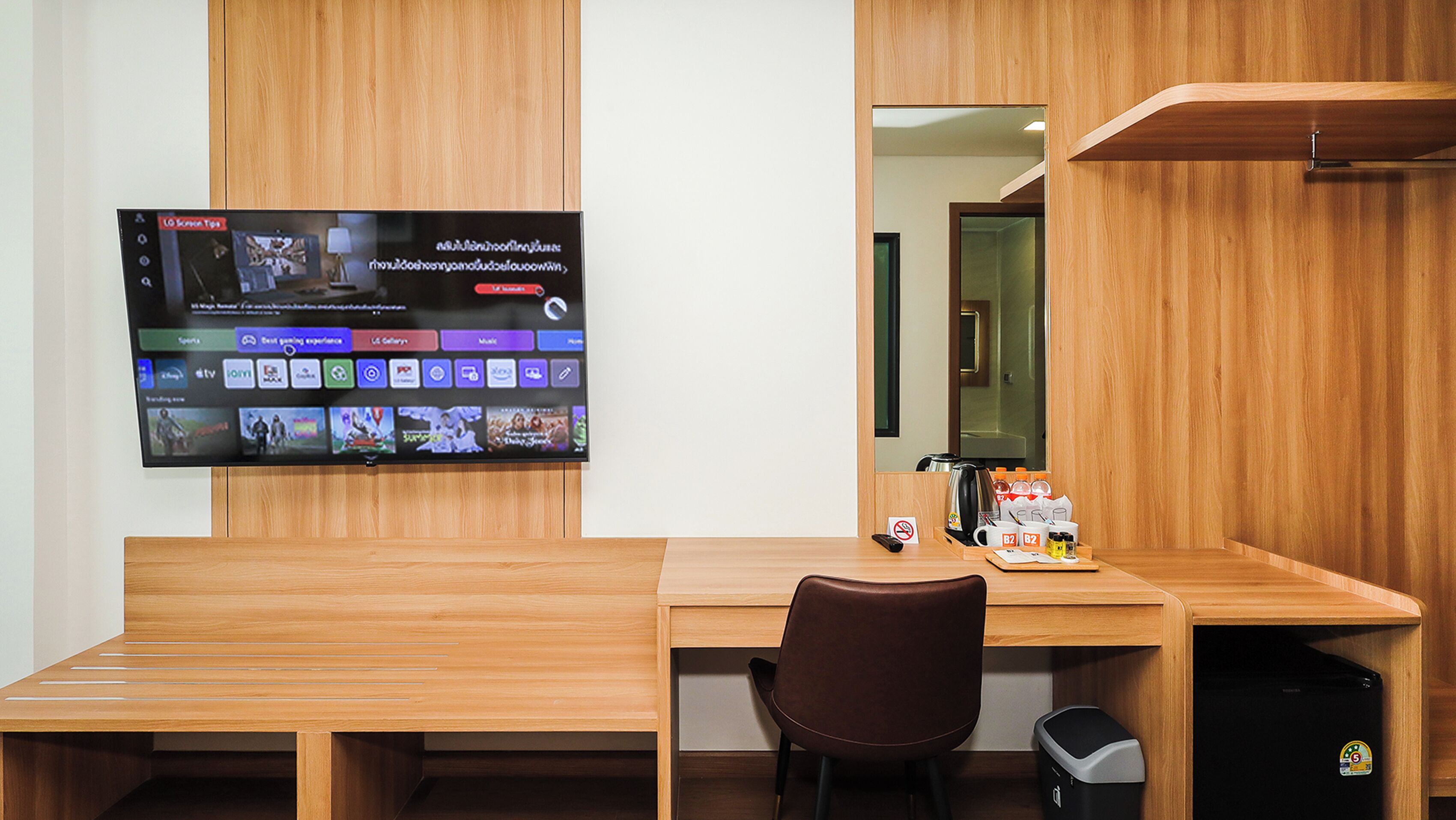 Habitación de hotel con escritorio de madera, un televisor en la pared mostrando varios canales, una silla, cafetera y un cesto de basura.