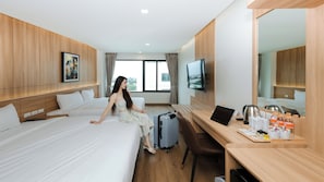 A hotel room with two beds, a desk with a laptop, a TV, and a view of the city.