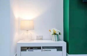 A white bedside table with a lamp, a vase with flowers, and a drawer labeled 'PARIS' and 'LONDON'. - Games Room, Stylish Home, Prime Location, Sleeps (Salford)