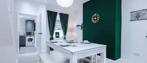 A modern dining area with a white table set for four, a green accent wall, and a clock.