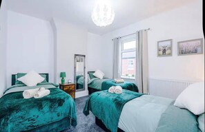 A hotel room with two beds, a mirror, a window with curtains, and artwork on the wall. - Games Room, Stylish Home, Prime Location, Sleeps (Salford)