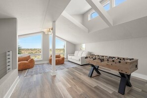 Ein modernes Zimmer mit Kicker, einem weißen Sofa und Blick auf die Wüste durch große Fenster.