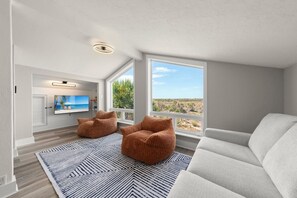 A modern living room with a large TV, two bean bag chairs, a white sofa, and a view of a desert landscape. - Sanibel Beach Retreat + Bonus Bungalow! Sleeps 17 • Private Pool (Sanibel)