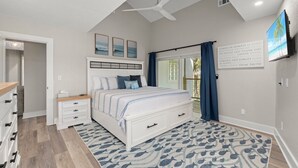 A bedroom with a bed, bedside tables, a ceiling fan, a window with curtains, and a motivational quote on the wall. - Sanibel Beach Retreat + Bonus Bungalow! Sleeps 17 • Private Pool (Sanibel)