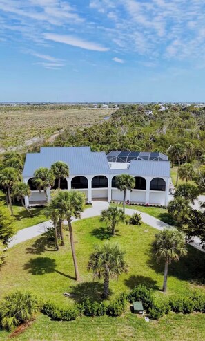 A modern building with a flat roof and multiple arched windows, surrounded by well-maintained grass and palm trees. - Sanibel Beach Retreat + Bonus Bungalow! Sleeps 17 • Private Pool (Sanibel)