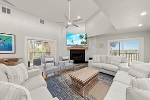 A modern living room with a fireplace, a ceiling fan, and a large TV. - Sanibel Beach Retreat + Bonus Bungalow! Sleeps 17 • Private Pool (Sanibel)