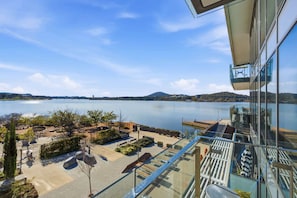 A modern building with a glass balcony overlooking a calm lake and distant hills. - Waterfront 1-Bed Apartment in Kingston (Kingston)