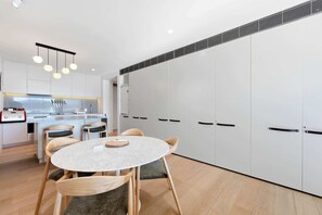 A modern kitchen with white cabinets, a dining area with a round table and chairs, and a built-in oven. - Waterfront 1-Bed Apartment in Kingston (Kingston)