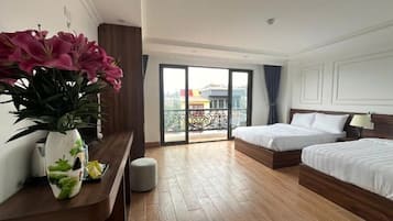 A hotel room with two beds, a wooden floor, a balcony with a view, and a vase with flowers on the nightstand.