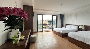 Habitación de hotel con dos camas, piso de madera, balcón con vistas y un florero con flores en la mesita de noche.