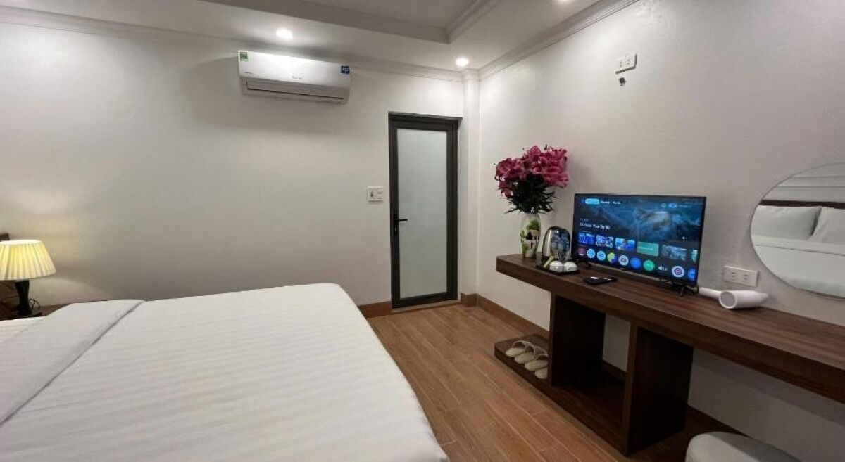 A hotel room with a bed, a desk with a computer, a TV, and a door.