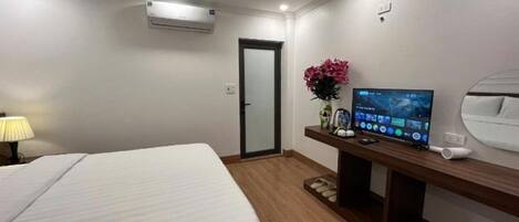A hotel room with a bed, a desk with a computer, a TV, and a door.