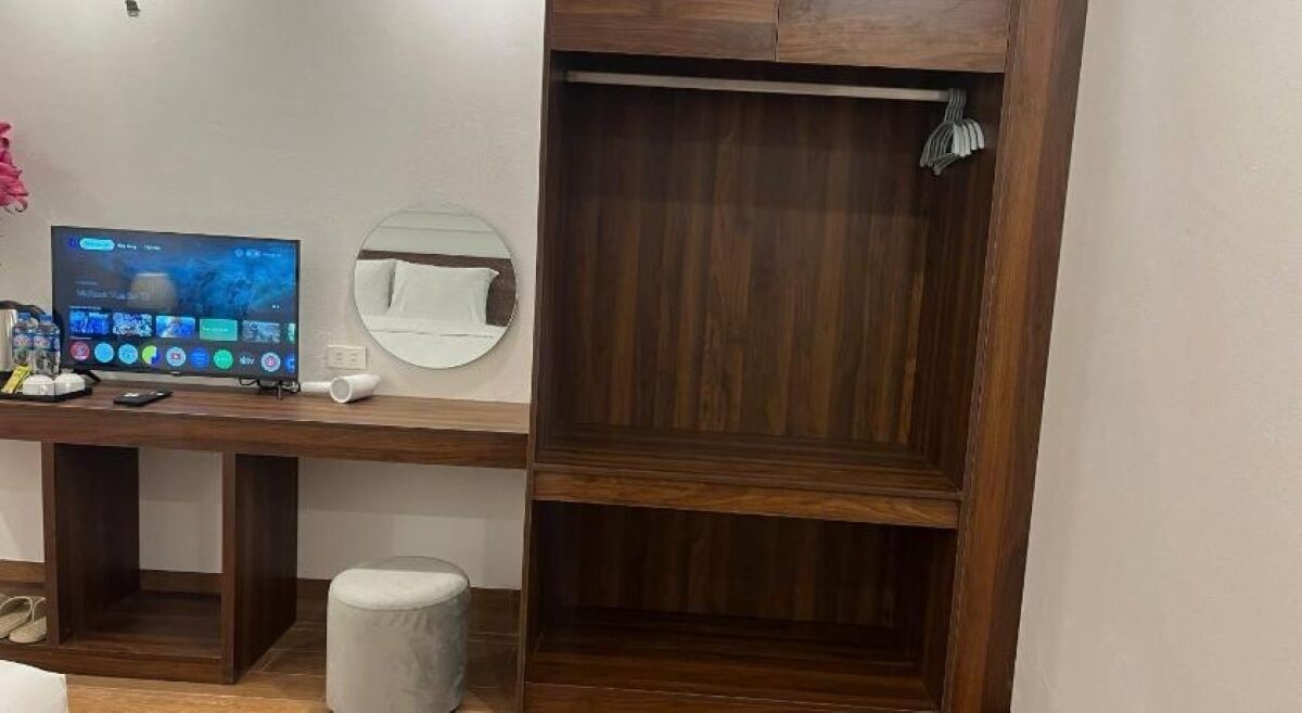 Una habitación con un escritorio de madera, televisor, una silla blanca y un armario de madera.