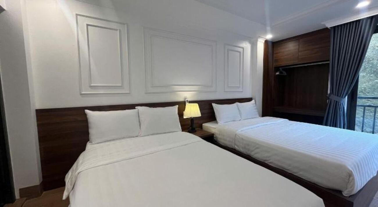 Habitación de hotel con dos camas, una mesita de noche con lámpara y una ventana con cortinas.